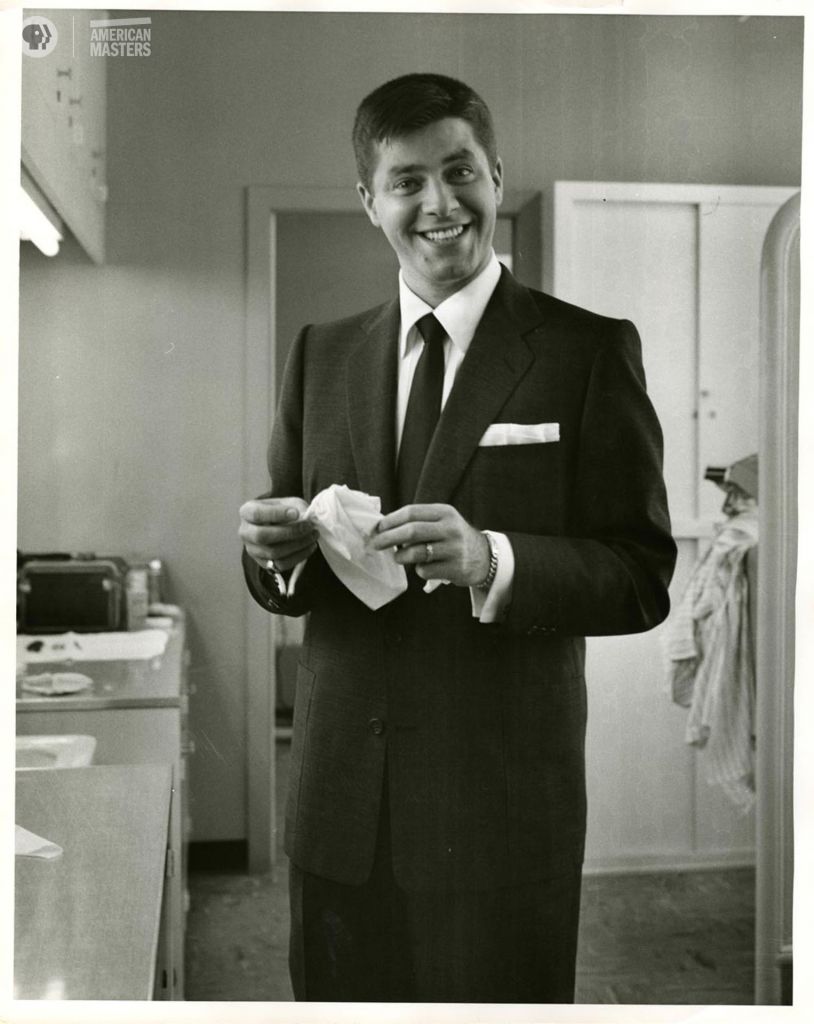 Jerry Lewis in the kitchen holding paper and smiling at the camera.