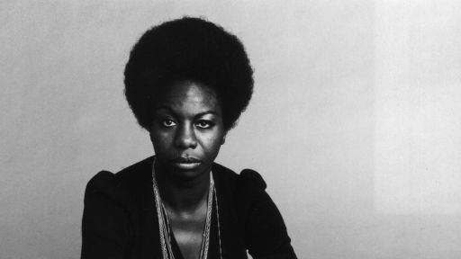 Full-length portrait of American vocalist Nina Simone (1933 - 2003) sitting cross-legged with a serious expression.