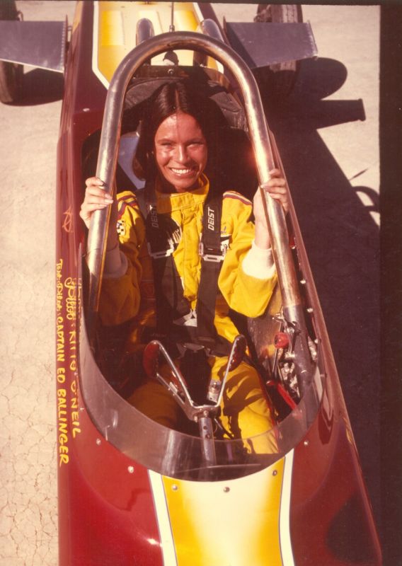 Smiling woman in a yellow racing suit sitting in a racecar