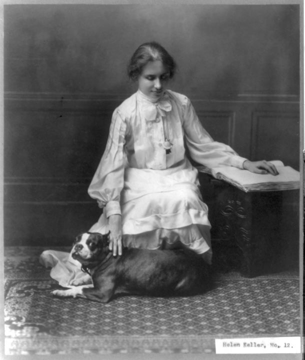 Helen Keller reading a braille book while petting a dog.