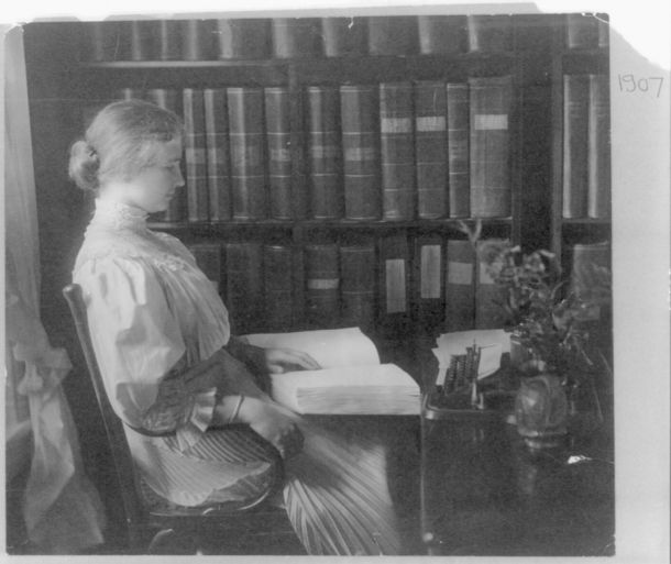 Helen Keller reading a braille book in a library.